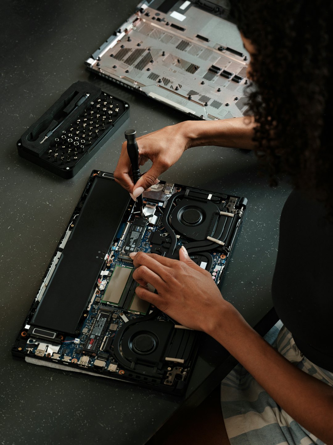 Mani che riparano un laptop aperto con un cacciavite e una scheda elettronica.